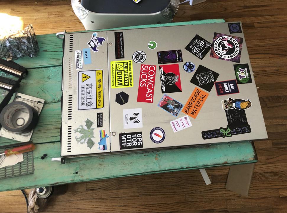 1u laying next to empty anti-static bags, duct tape, and a glossy plastic PowerMac G4. goodnight white pride sticker. tor sticker. riseup.net sticker. old defcon sticker. chinese high voltage warning sticker. food not bombs sticker. comcast sucks sticker. eliminate DRM sticker. docker nyan cat sticker. 